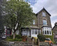 An exterior view of a large Lakeland stone property in windermere with parking.