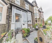 An exterior view of the four star Abacus House, a traditional Lakeland stone property, the garden in the foreground also contains seating.