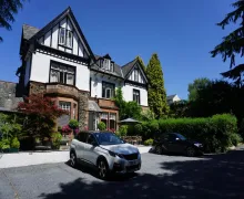 An external view of the four-star Dene House Guest House in Bowness-on-Windermere. the property has a Lakeland stone lower section with a white render and black beams on the upper section.