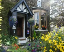An exterior image of the Denehurst Guest House with pretty flowerbeds at the front of the Lakland Stone built property.