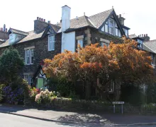 An external image of the four-star Kirkwood Guest House near Windermere, a Lakeland stone property partially shaded by ornamental trees.