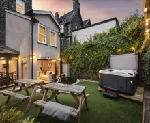 An exterior rear garden image of the  Rosemount Lake District Townhouse with the house in the background and a lawned area with seating and a Hot Tub.