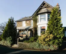 An exterior view of the Rum Doodle, Windermere B&B, a traditional Lakeland stone property with mature trees in the front garden.